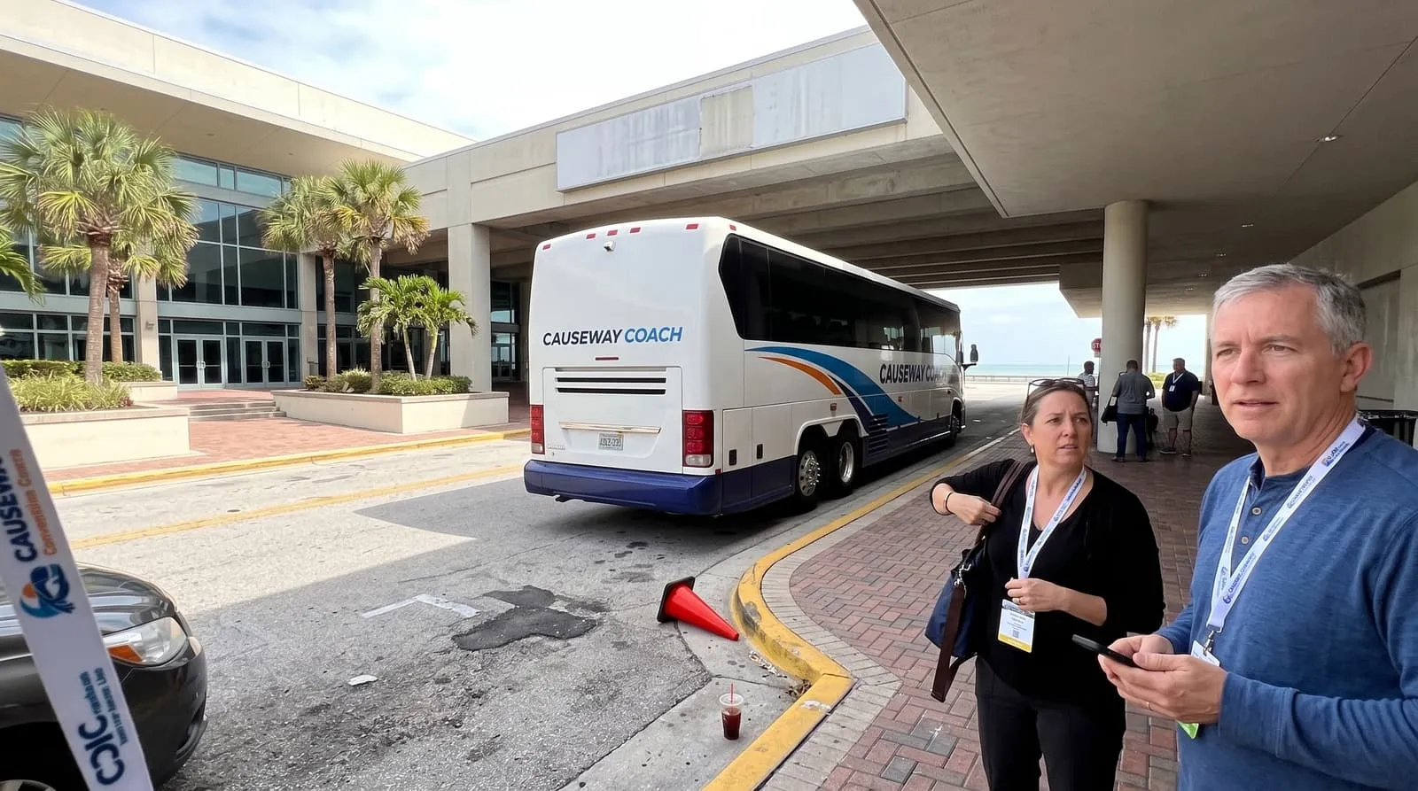 Two conference delegates with lanyards beside a Causeway Coach motorcoach outside the beachside convention centre in Daytona Beach