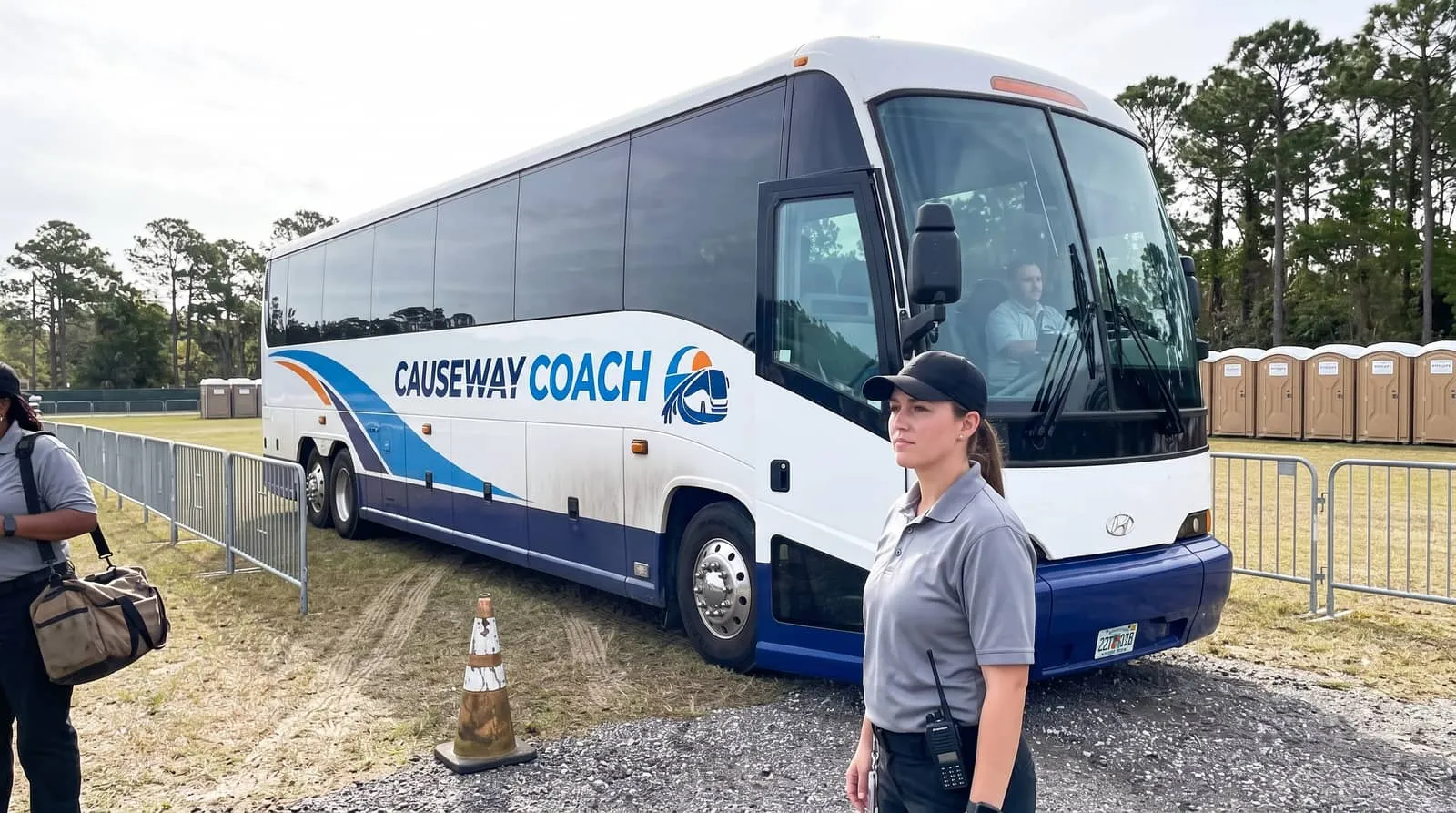 An event staff member with a radio at the door of a Causeway Coach shuttle in a temporary staff parking area near Daytona Beach