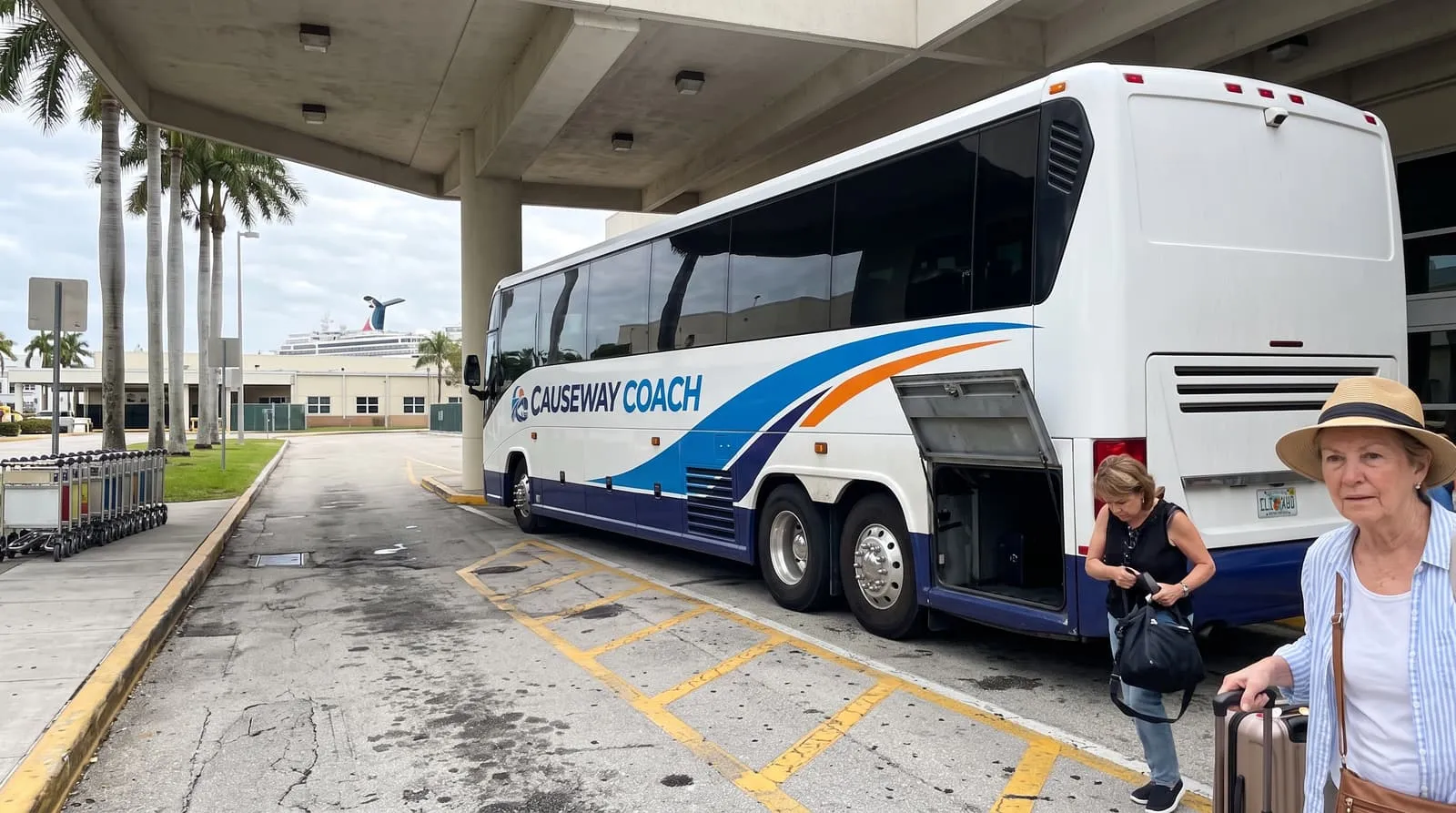 A traveller with a suitcase beside a Causeway Coach motorcoach at the ground transport island outside Fort Lauderdale airport