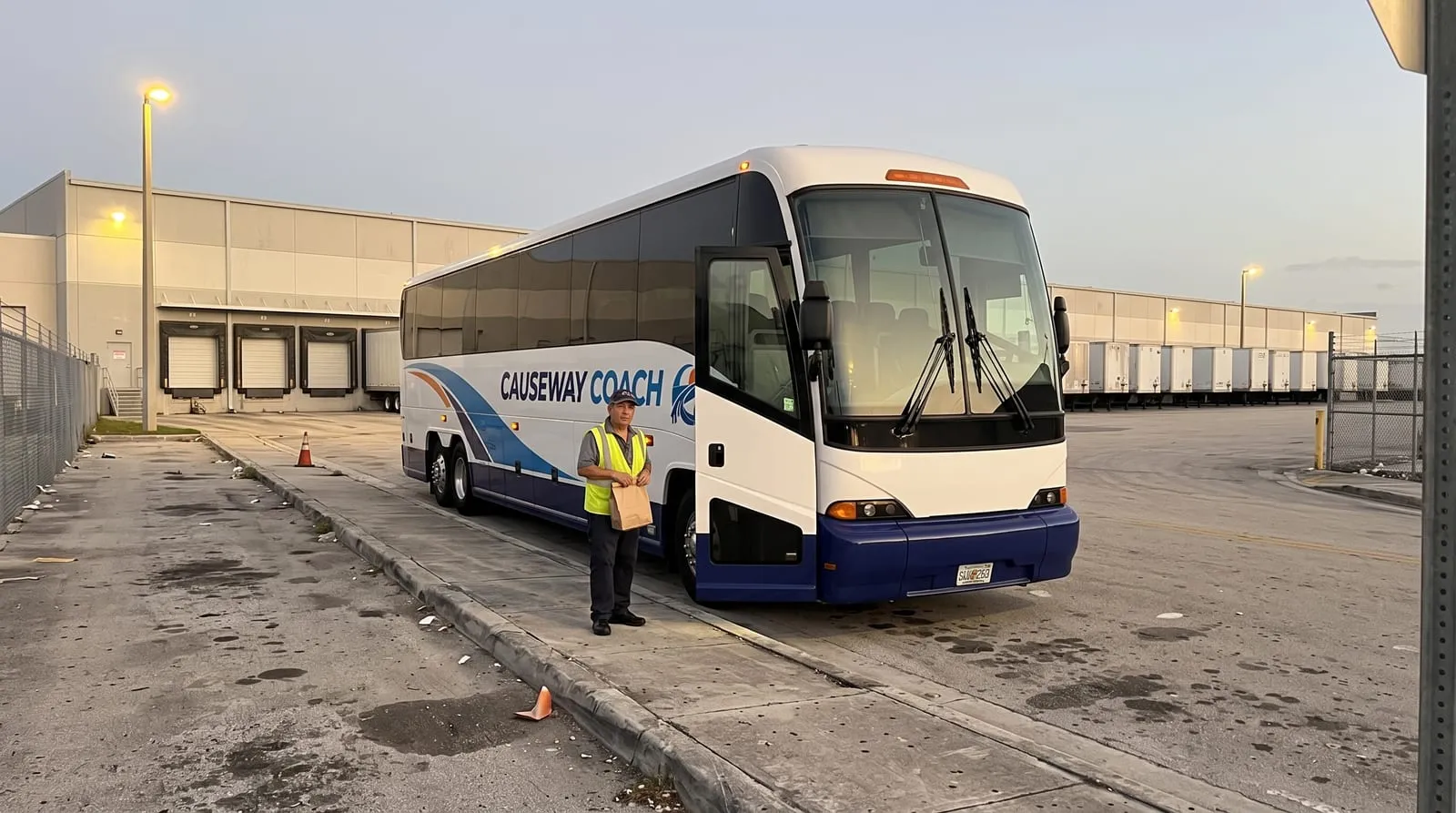 A shift worker in a hi-vis vest boarding a Causeway Coach shuttle in a Doral cargo district before dawn
